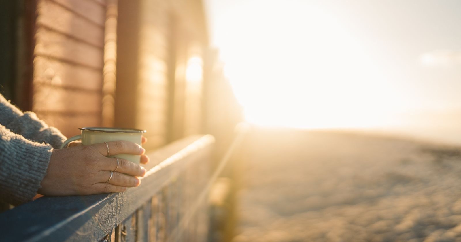 A hand holding a mug on a porch railing in warm morning sunlight