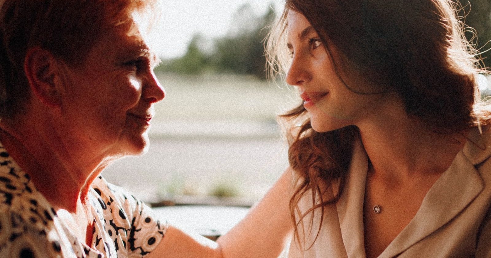 An older mother and her adult daughter smiling at each other across a table