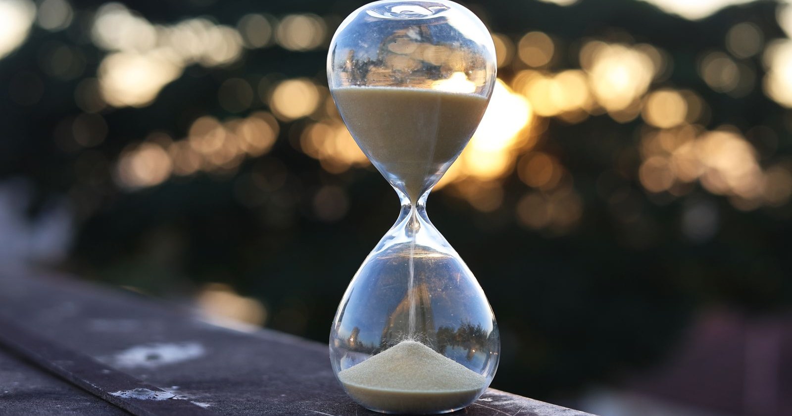 An hourglass with sand running through it on a ledge at sunset