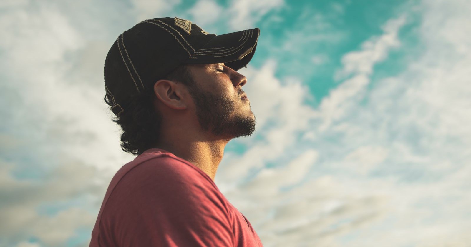 A man with his eyes closed taking a calm breath under a cloudy sky