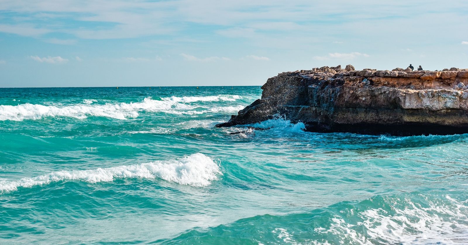 Waves breaking against a rocky headland under a clear sky